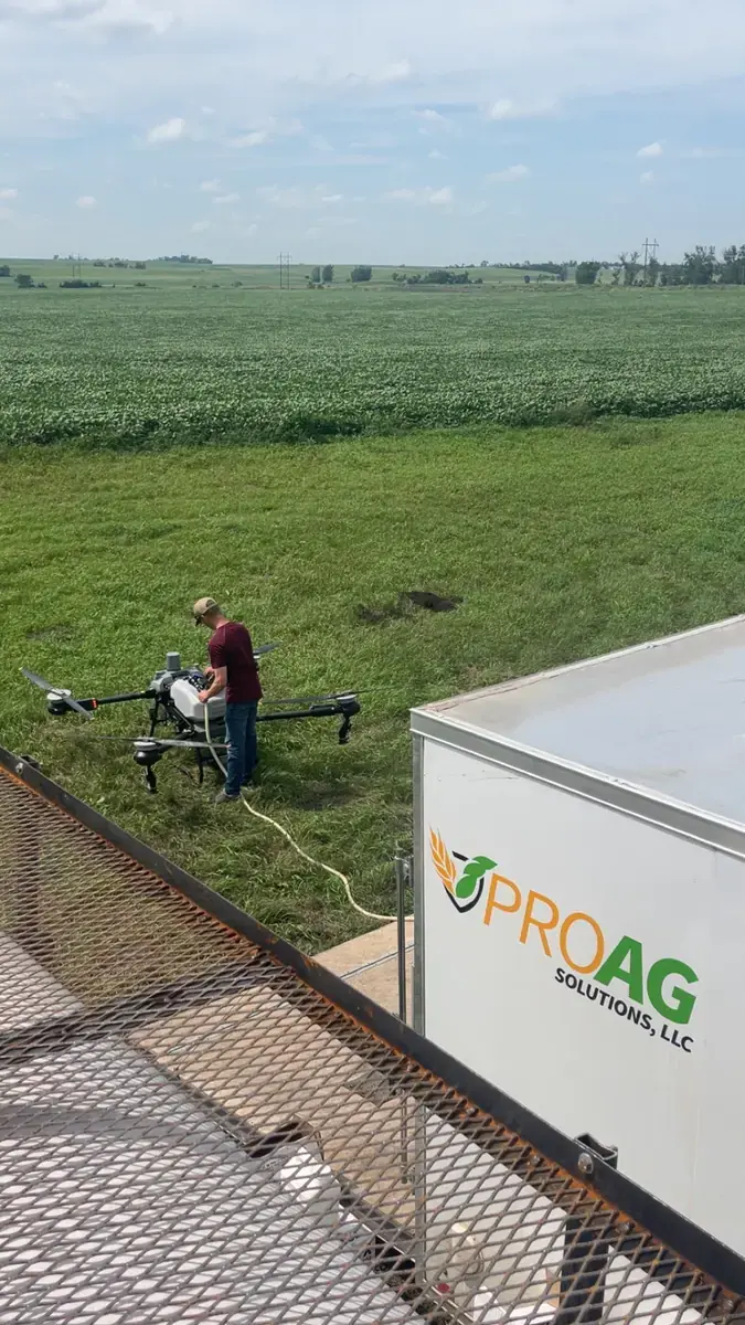 Pro Ag Solutions pilot refilling a DJI Agras spray drone next to the company's branded trailer at a North Dakota soybean field